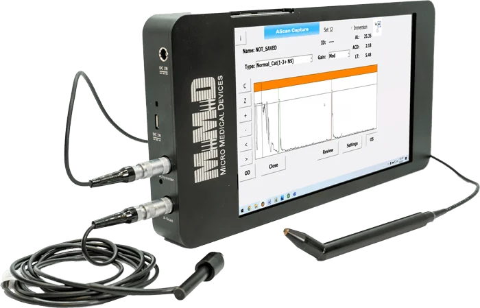 A black medical diagnostic device with a touchscreen displaying a data graph and medical readings, connected to cables and a pen-like sensor. The device is labeled Micro Medical Devices.