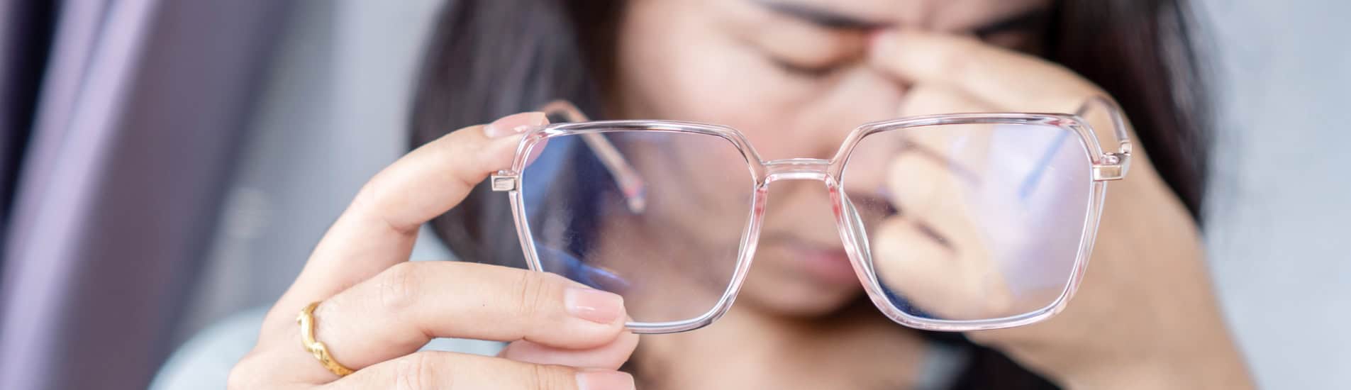 A woman experiencing eye strain while holding eyeglasses.